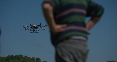 An innovative farmer operates a drone while standing in the middle of a field at sunset, using aerial technology to survey crops and monitor farmland as part of modern smart farming practices. video
