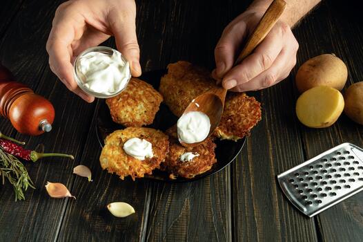 Adding sour cream to pancakes with a spoon in the hands of a man. Low key concept for preparing a vegetarian dinner. photo