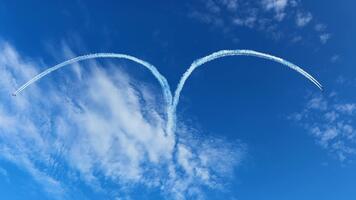 utomhus- flyg scen fångar ögonblick när flygplan lämna symmetrisk rökig mönster liknar hjärta, rik himmel toner och svag moln skapa dynamisk bakgrund för kreativ luft visa. video
