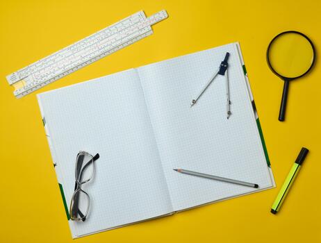 A large notebook for notes and drafting with stationery objects for a student on a yellow background. Ruler, marker, pencil, magnifying glass, compasses, glasses. Top view. photo