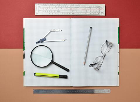 A large notebook for notes and drafting with stationery objects for a student. Ruler, marker, pencil, magnifying glass, compasses, glasses. Top view. photo