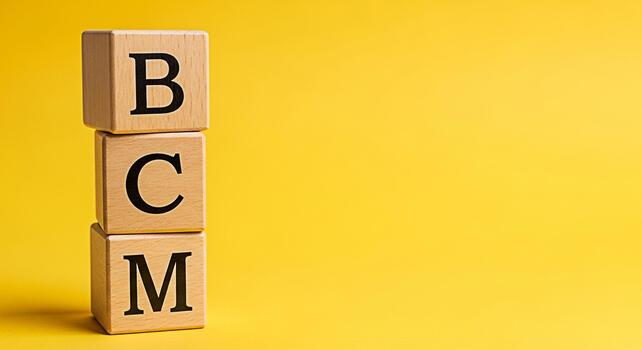 Stacked wooden blocks displaying BCM against a vibrant yellow background symbolizing business continuity management and strategic planning for risk mitigation and organizational resilience in a dynami photo