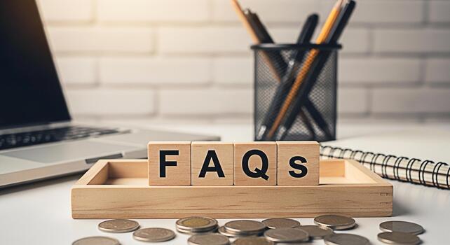 Wooden blocks spelling FAQs displayed on a bright white desk with laptop pens and coins representing frequently asked questions and information resources in a modern business setting photo
