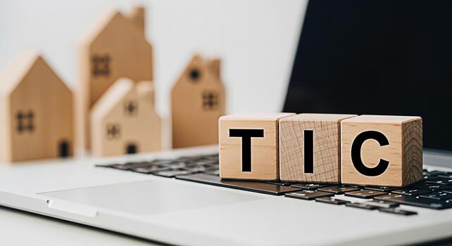 Wooden blocks spelling TIC on a laptop keyboard with miniature house models in the background representing tenancy in common and real estate investment in a modern techdriven environment photo