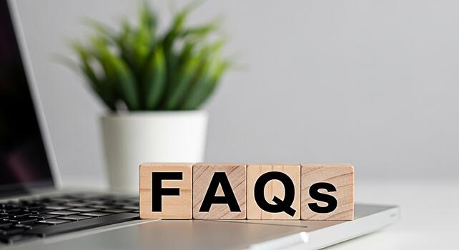 Wooden blocks displaying FAQs on a laptop keyboard in a bright office setting symbolizing readily available information and customer support for online queries and common questions photo