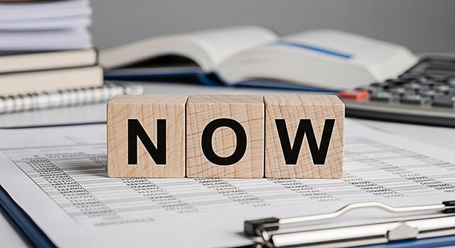 Wooden blocks spelling NOW resting on financial documents in a bright office setting symbolizing urgency and immediate action in business and investment decisions for success and growth photo