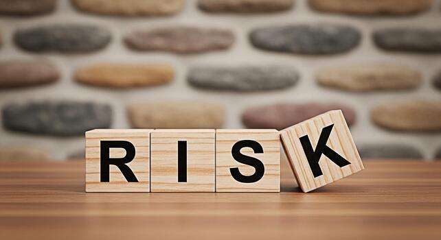 Wooden blocks spelling RISK on a wooden surface with one block tilted against a textured stone wall conveying a sense of uncertainty challenge and the potential for both loss and gain in business photo