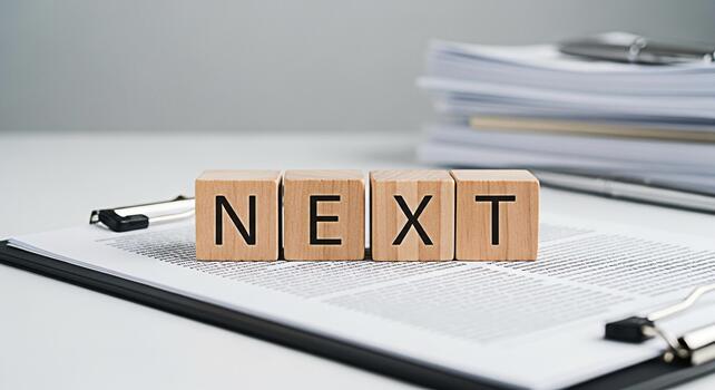 Wooden blocks spelling NEXT resting on a clipboard with documents in a bright office symbolizing future plans upcoming projects and the anticipation of new opportunities in business and personal devel photo
