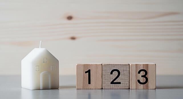 Minimalist house candle and wooden blocks displaying numbers on a neutral surface symbolizing simplicity counting and the concept of home ownership in a serene and uncluttered setting photo