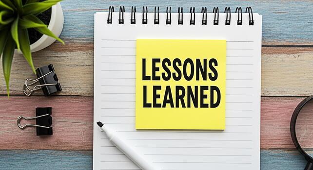 Lessons learned concept Notepad with yellow sticky note displaying Lessons Learned on a wooden desk with a plant pen paper clips and magnifying glass symbolizing reflection and knowledge acquisition photo