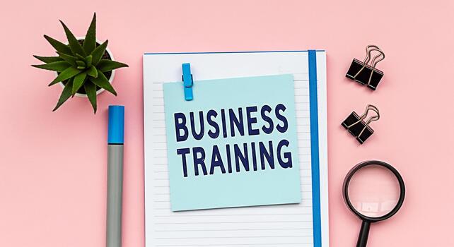 Overhead shot of business training note on a notebook with a pen plant magnifying glass and binder clips on a pink desk representing learning and development in a creative and organized workspace photo