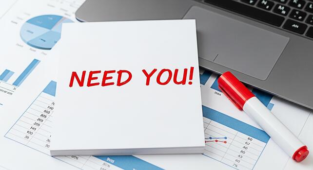 Urgent request for assistance A stack of notes with NEED YOU written in red marker placed on top of financial charts and a laptop conveying a sense of urgency and immediate need for help photo