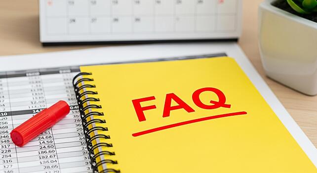Yellow notebook displaying FAQ on a wooden desk with financial reports a calendar and a potted plant symbolizing readily available information and customer support in a bright and organized office set photo