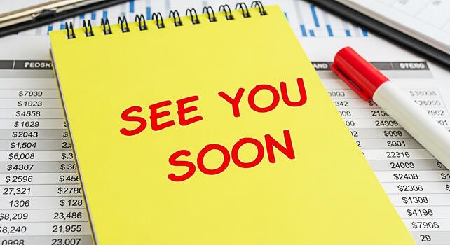 Bright yellow notepad displaying See You Soon in a financial setting symbolizing anticipation and future collaboration within a business environment fostering a positive and optimistic mood for upcomi photo