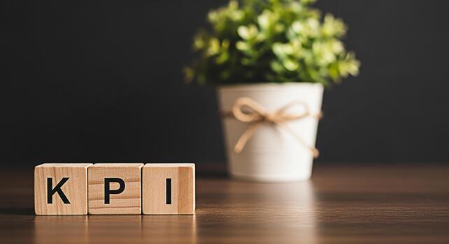 Wooden blocks spelling KPI on a wooden table with a blurred potted plant in the background representing key performance indicators and business success in a professional and minimalist setting photo