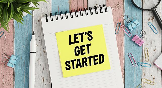 Bright yellow sticky note exclaiming Lets Get Started on a notebook surrounded by colorful paper clips on a rustic wooden desk conveying motivation and a fresh start for new projects photo