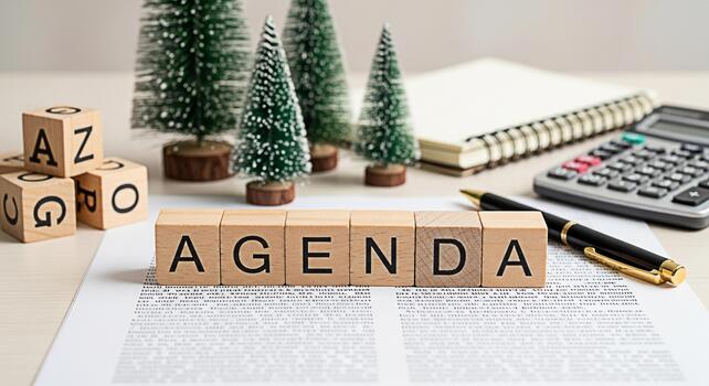 Wooden blocks spelling Agenda resting on a document in a bright office setting surrounded by miniature Christmas trees a calculator and a notepad conveying a sense of organization and planning for the photo