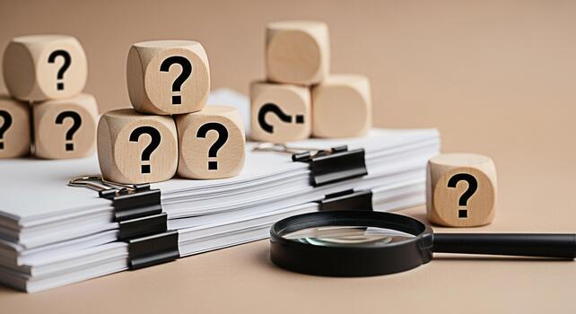 Wooden question mark blocks stacked on a pile of documents with a magnifying glass in a neutral setting representing uncertainty investigation and the search for answers in business and research conte photo