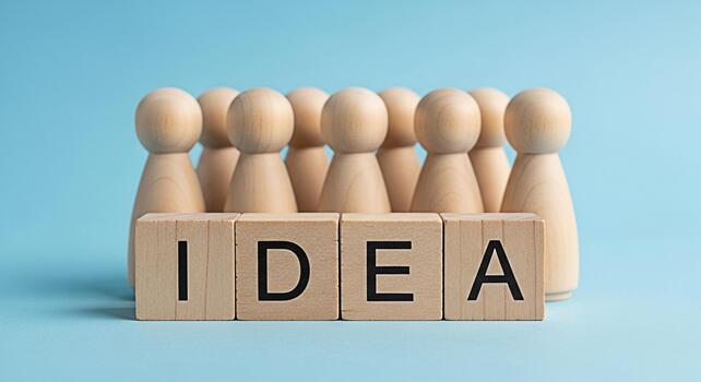 Wooden figures standing behind blocks spelling IDEA on a light blue background representing teamwork brainstorming and the generation of creative solutions in a collaborative environment photo