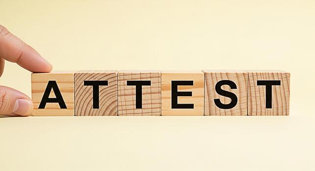 Hand arranging wooden blocks spelling ATTEST on a light yellow background conveying a sense of verification confirmation and legal declaration in a clean and minimalist setting photo