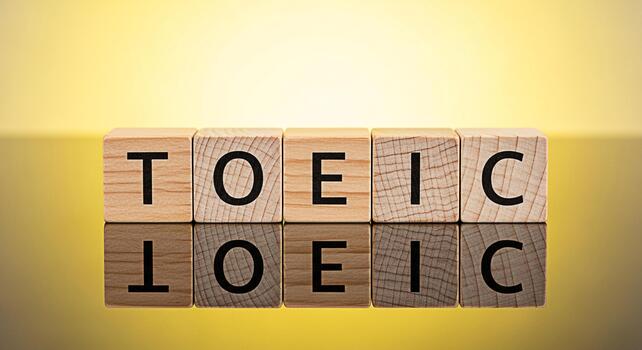 Wooden blocks spelling TOEIC on a reflective surface against a soft yellow background representing the concept of English language proficiency and educational assessment for global communication skill photo
