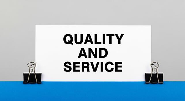 Closeup of a paper sheet displaying Quality and Service in bold letters held by binder clips on a blue surface against a gray background emphasizing business values and customer satisfaction photo