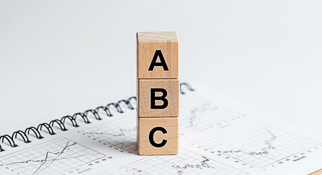 Wooden ABC blocks stacked on a spiral notebook with financial charts representing basic concepts in business analytics and education in a clean minimalist and bright studio setting photo