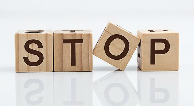 Wooden blocks spelling STOP one block tilting on a white reflective surface conveying a message of caution halt and prevention in a clean minimalist setting symbolizing control and decisionmaking photo