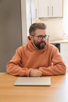 Man sitting at table with closed laptop. Concept of work pause, thinking, remote job routine, and moment of reflection during daily digital workflow. photo