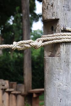 Natural fiber rope with an intricate knot firmly securing rustic wooden structure outdoors. Durable texture and reliable connection create stable, enduring bond. robust construction evokes playful photo