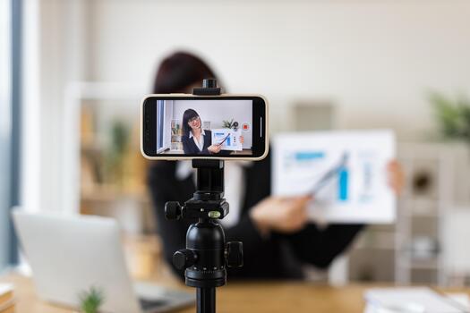 Caucasian woman recording business blog using smartphone on tripod in office environment. Discussing chart data in . Professional creating online content. Relates to business, content creation. photo