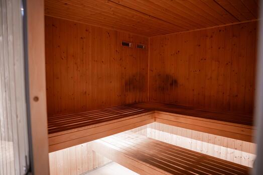 Tiered pine benches wrap a corner, lit from below with soft diffuse light. Modern spa sauna in Mellieha, Malta sits empty and clean, with minimal warm tones. photo