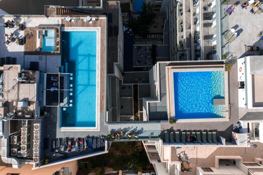 Aerial top view shows two rooftop pools linked by a pedestrian bridge in Mellieha, Malta. Midday light casts sharp shadows, highlighting geometry and patterns. photo