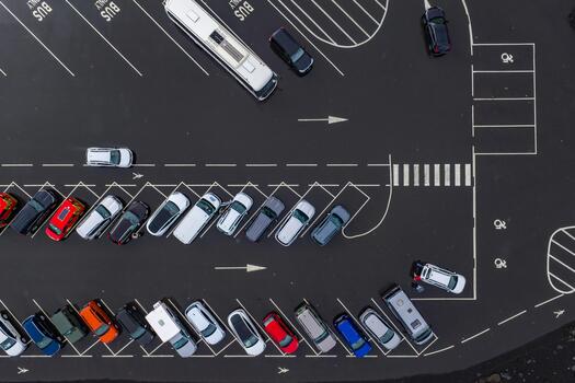 Aerial top down view of a marked parking lot in Iceland with angled spaces, BUS bays, a crosswalk, arrows, and mixed vehicles under overcast light, showing ordered patterns. photo