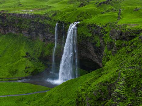Aerial view shows Seljalandsfoss on Iceland South Coast, white water drops over mossy basalt into a shallow pool, footpath and recess behind the falls are visible in soft light. photo