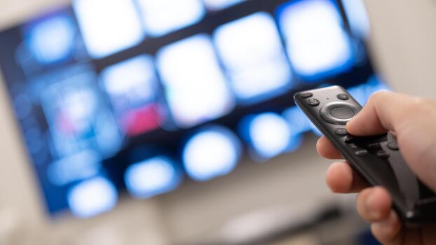 A focused view of a TV remote being used to control content on a smart TV with icon tiles blurred in background. photo