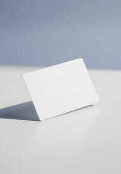 Blank white card casting a shadow on a white surface with a light blue backdrop, studio lighting photo