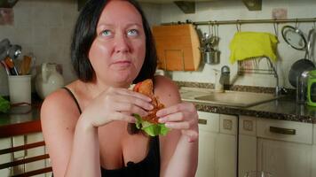 mulher dentro Preto tanque topo detém e prepara para comer apetitoso hamburguer com sésamo pão, fresco alface, queijo em branco prato ao lado Sombrio bebida. video