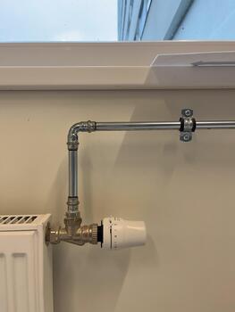 Radiator valve and pipe system mounted on wall, showcasing temperature regulation mechanism in a modern heating environment with sleek design and functionality photo