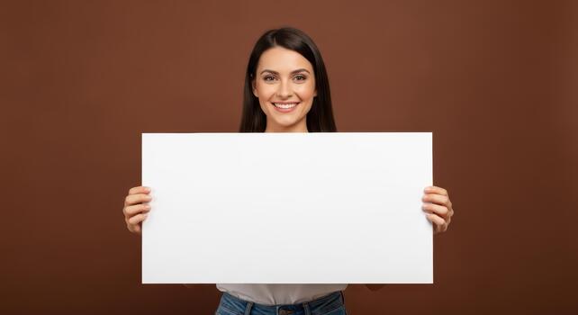 Smiling woman holding a blank white sign in front of a brown background looking at the camera photo