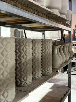 Ceramic vases and planters shaped from clay are neatly arranged on shelves in a pottery workshop, showcasing different motifs and styles photo