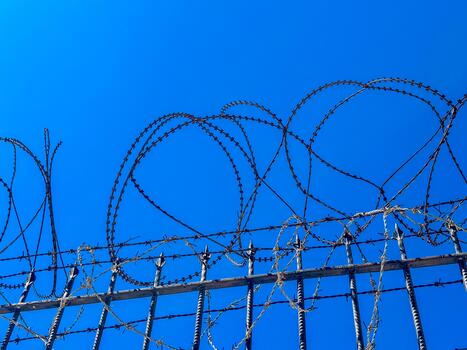 Barbed wire fence against a clear blue sky. sharp edges of the wire create a stark contrast with the bright background, symbolizing security and confinement photo