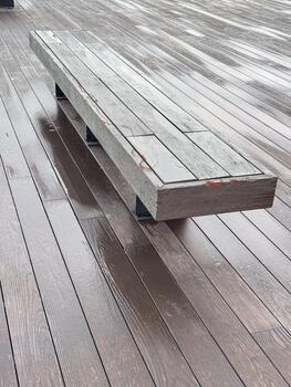 A wooden bench on a wet wooden deck. The surface is shiny from rain, creating a reflective effect. The scene is calm and minimalistic. photo