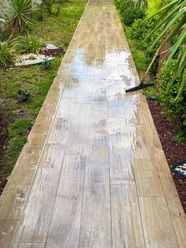 A clean, wet stone pathway lined with greenery. The path is made of large tiles and is surrounded by plants and grass. photo