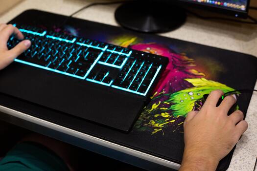 cerca arriba de mano utilizando ratón en juego de azar alfombrilla de ratón con vibrante colores, iluminado teclado con azul iluminar desde el fondo. moderno juego de azar preparar en hogar oficina escritorio foto