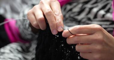 en person användningar nålar och garn. svart garn är interlaced in i en design. de fokus är på de händer och de spela teater av skapande något mjuk och värma. video