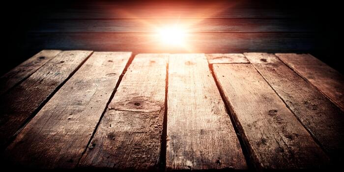 A rustic wooden table surface is illuminated by a warm glowing light from above against a dark background photo
