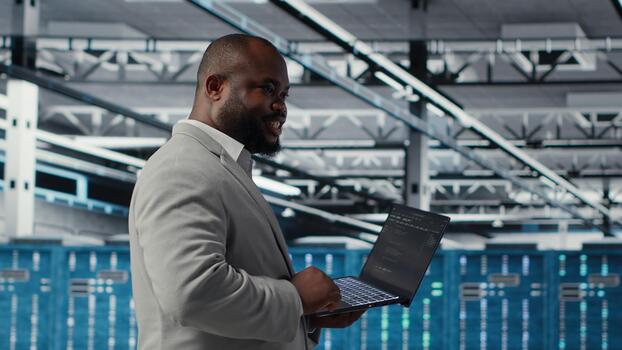 Cheerful data center system administrator reviews code for automation scripts. Jolly server room employee running diagnostics on equipment, doing predictive error detection, camera B photo