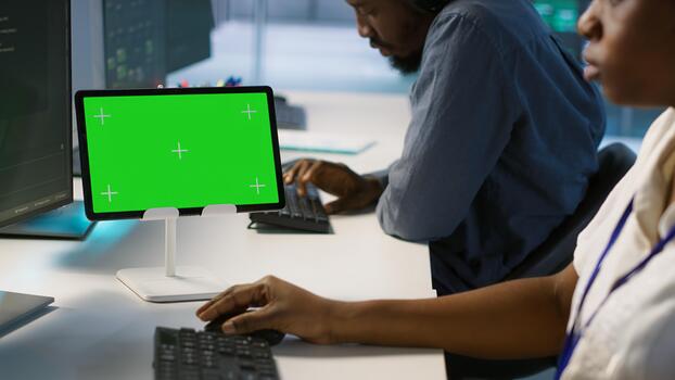 System administrator using isolated screen tablet, working in server farm to optimize it for data processing requirements. Software developer coding on chroma key device in data center, camera A photo
