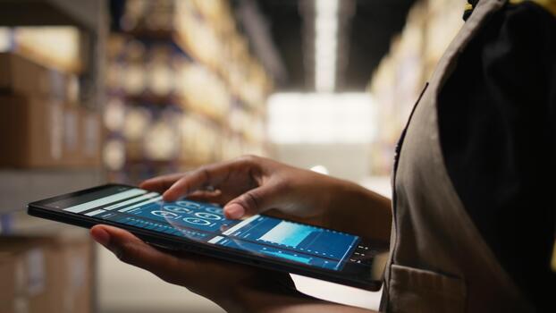 Close up of distribution hub worker overseeing supply chain process for e-commerce. Reviewing logistics and shipping data on tablet, updating tracking labels for order fulfillment. Camera A. photo